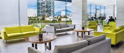 A modern lobby with a city view, featuring a yellow sofa, grey sofas, and green armchairs.