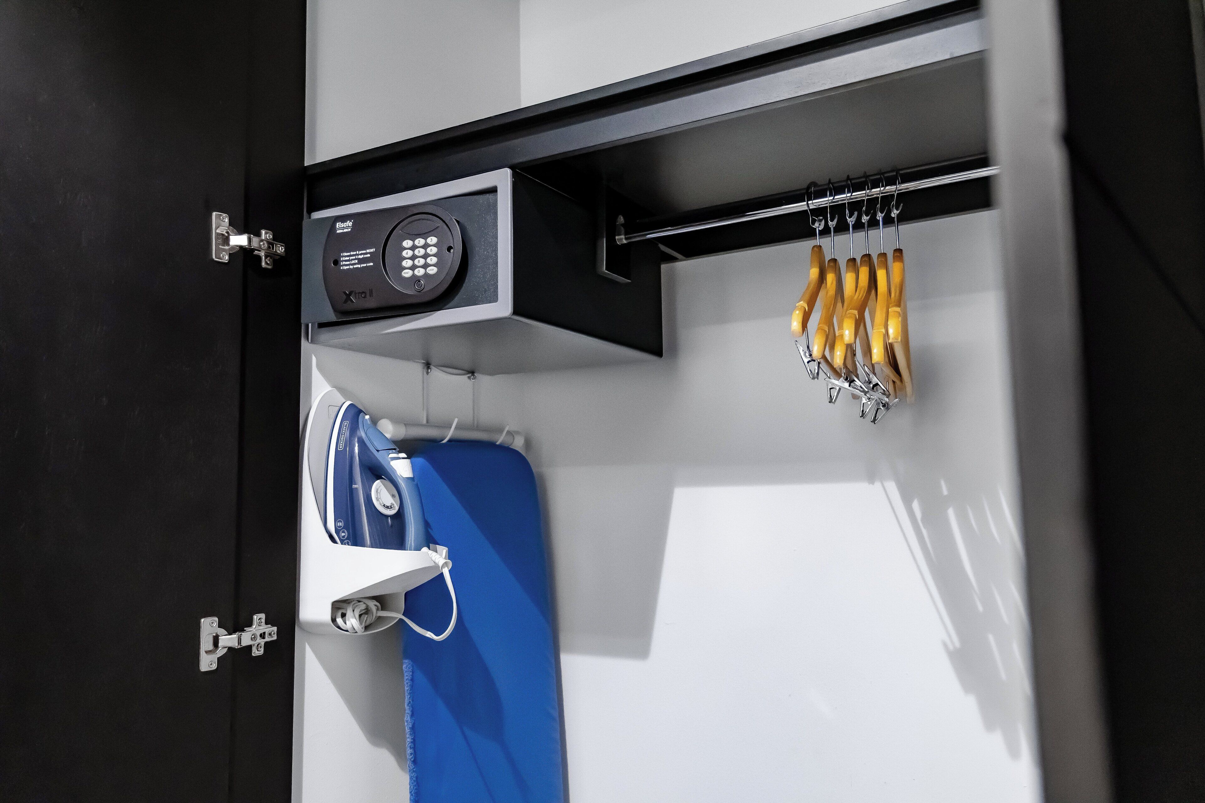 A hotel room with a black door, a blue suitcase, a white bag, and a set of yellow keys hanging on a hook.