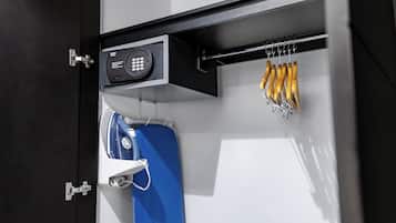 A hotel room with a black door, a blue suitcase, a white bag, and a set of yellow keys hanging on a hook.