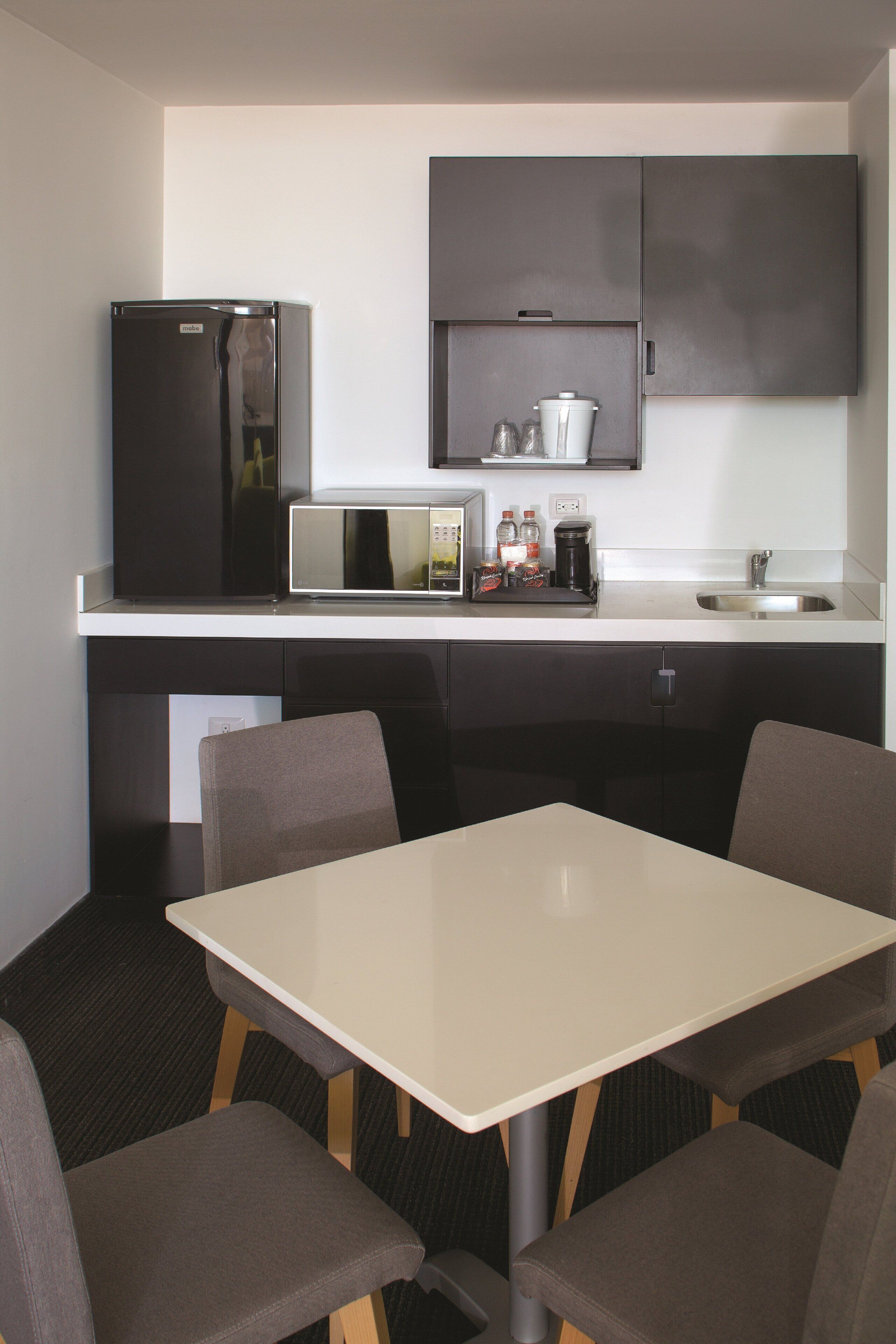 Una cocina compacta con refrigerador, microondas, cafetera y un lavamanos pequeño.