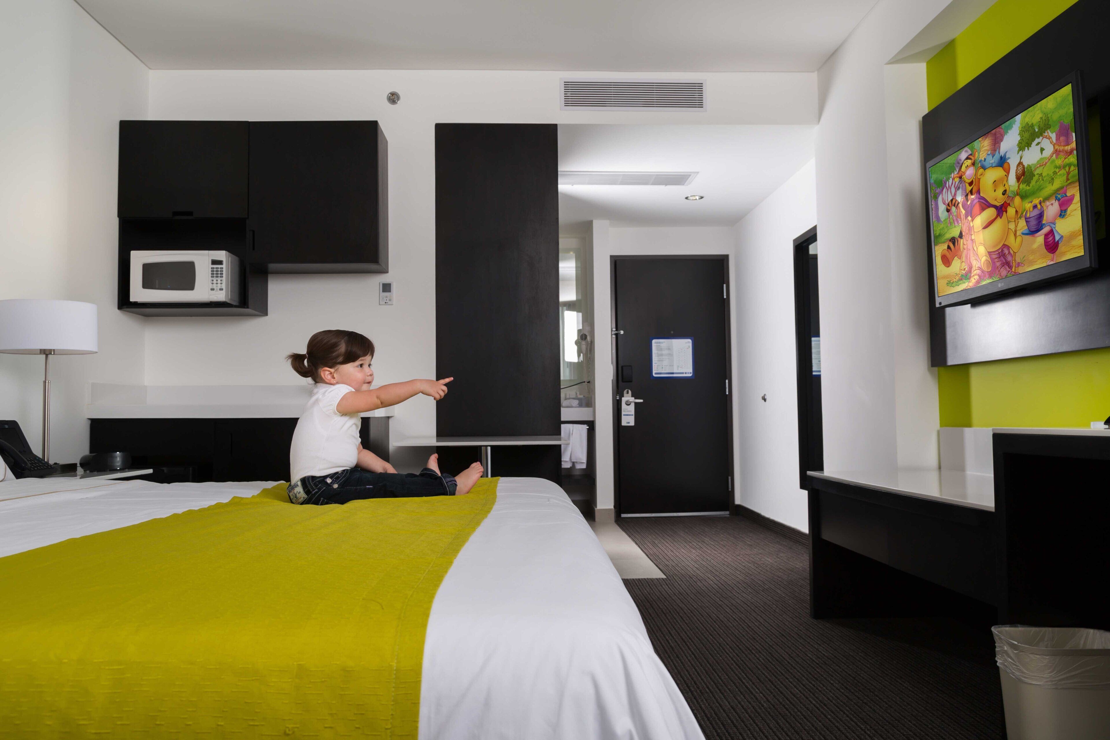 Una habitación de hotel con cama, televisor, microondas, escritorio y basurero.