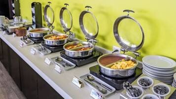 A buffet with multiple food stations, each with a metal lid and labeled with food names.