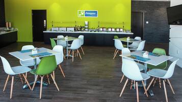 Un café moderne aux murs verts, avec une enseigne « Desayuno Express » et de nombreuses tables accompagnées de chaises.