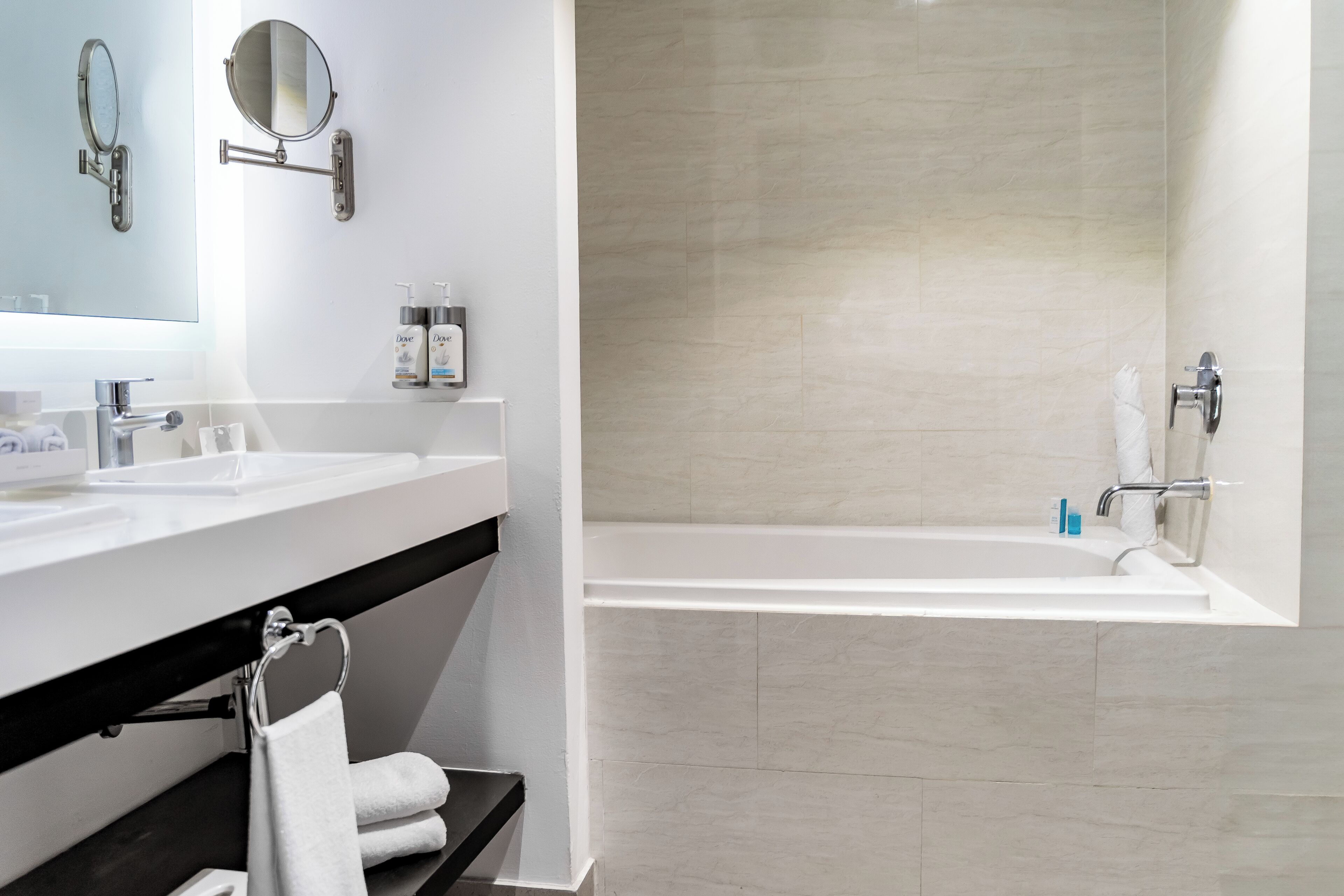 A modern bathroom with a white sink, two mirrors, a bathtub, and a towel rack.