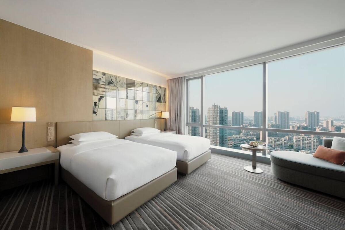 A hotel room with two beds, a sofa, a small table, and a city view.