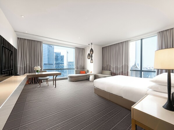 A modern hotel room with a large bed, a desk with a chair, a sofa, a TV, and a view of the cityscape. - Hyatt Regency Suzhou (Suzhou)