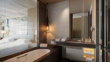 A modern bathroom with a large bathtub, a vanity with a mirror, and a window with blinds.