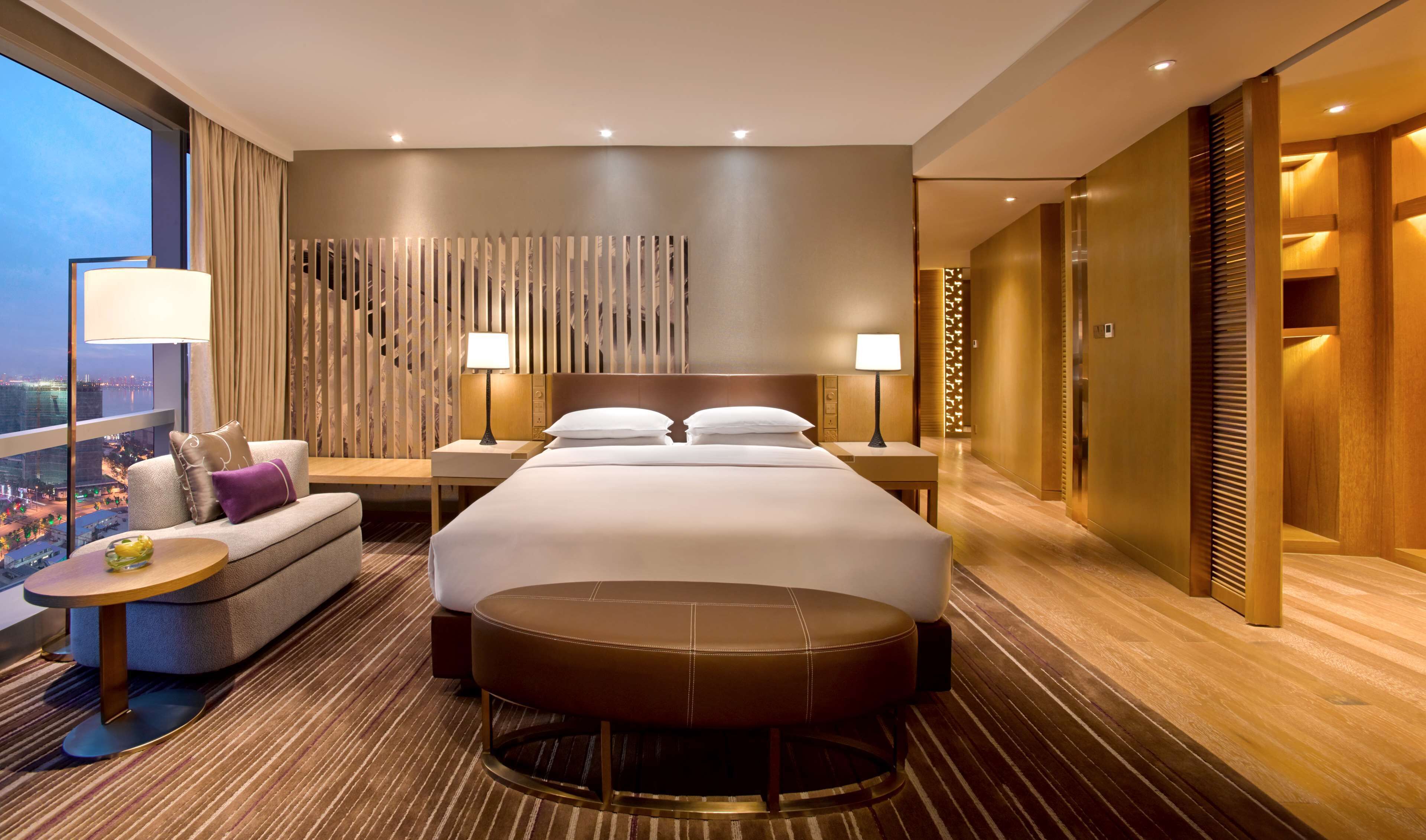 A modern hotel room with a large bed, a sofa, a small table, and a view of the city.
