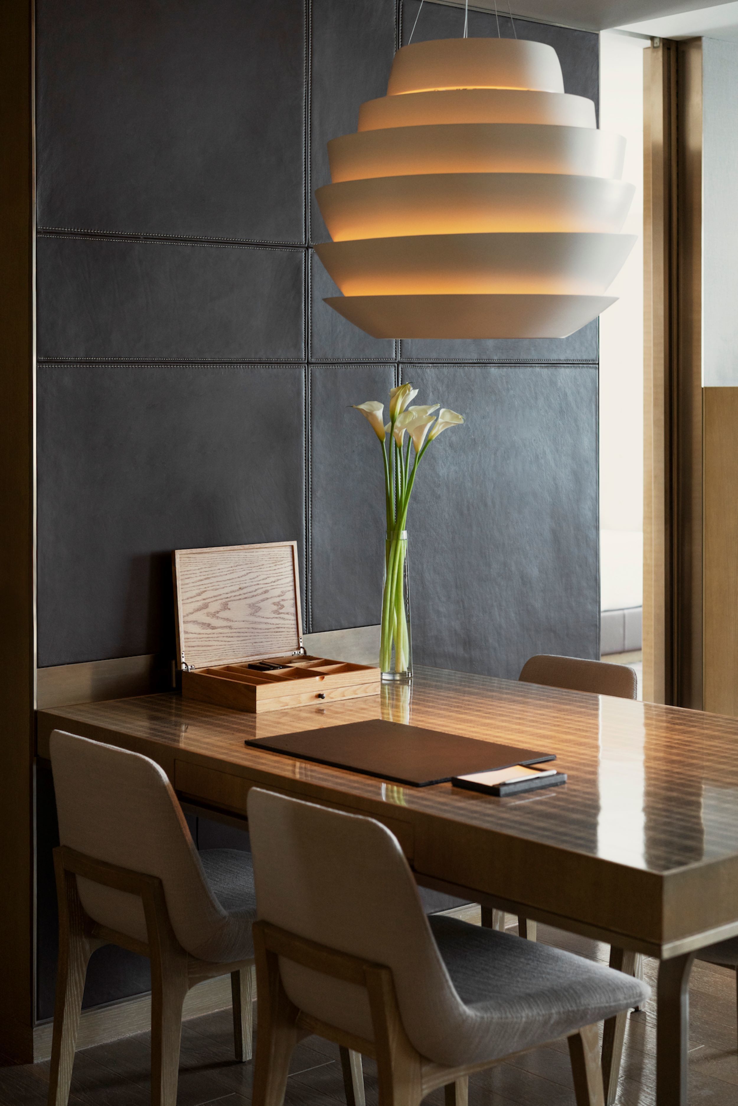 A modern dining area with a wooden table, cushioned chairs, a vase with flowers, and a unique pendant light.