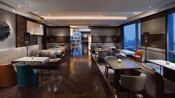 A modern hotel lobby with a herringbone wood floor, leather seating, and a city view through large windows.