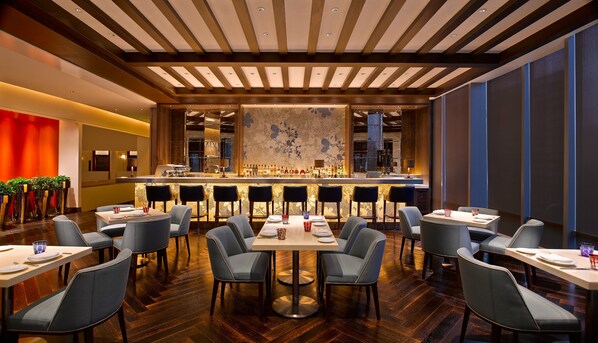 A modern bar area with a long counter, multiple seating options, and a patterned wall.