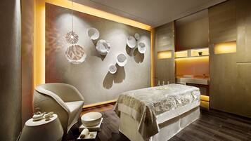 A modern hotel room with a bed, a chair, a small table, and a wall with decorative elements.