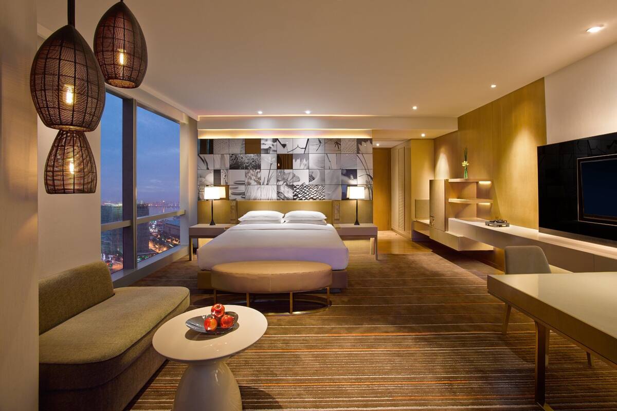 A modern hotel room with a large bed, two bedside tables, a TV, and a view of the cityscape.