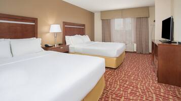 A hotel room with two beds, a desk with a television, a lamp, and a window with curtains.