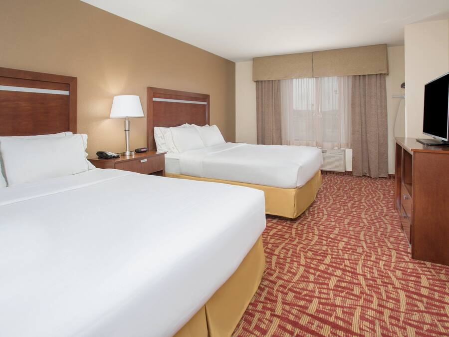 A hotel room with two beds, a desk with a television, a lamp, and a window with curtains.