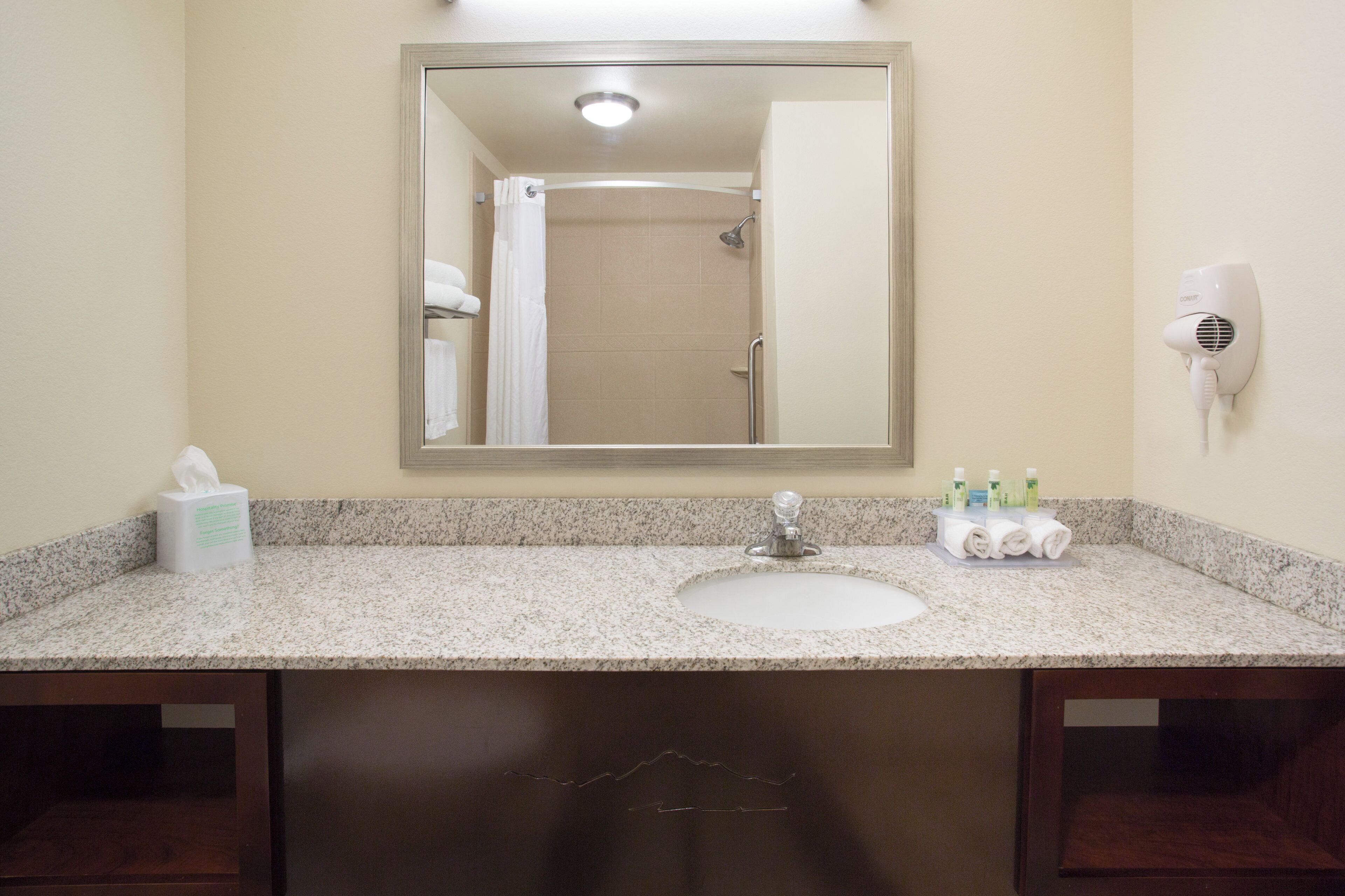 A bathroom with a sink, mirror, towel rack, and a hairdryer on the wall.