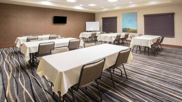 A conference room with multiple tables and chairs, a whiteboard, and a flat-screen TV on the wall.