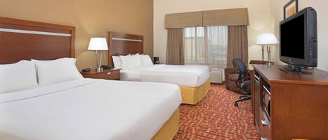 A hotel room with two beds, a desk, a television, and a window with curtains.