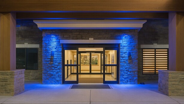 A hotel entrance with a stone facade, glass doors, and a blue-lit interior. - Holiday Inn Express & Suites Glendive by IHG (Glendive)