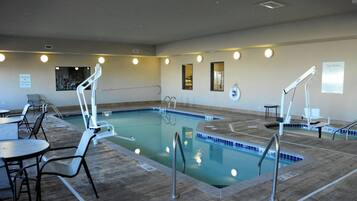 An indoor swimming pool with multiple lanes, safety railings, and lounge chairs.