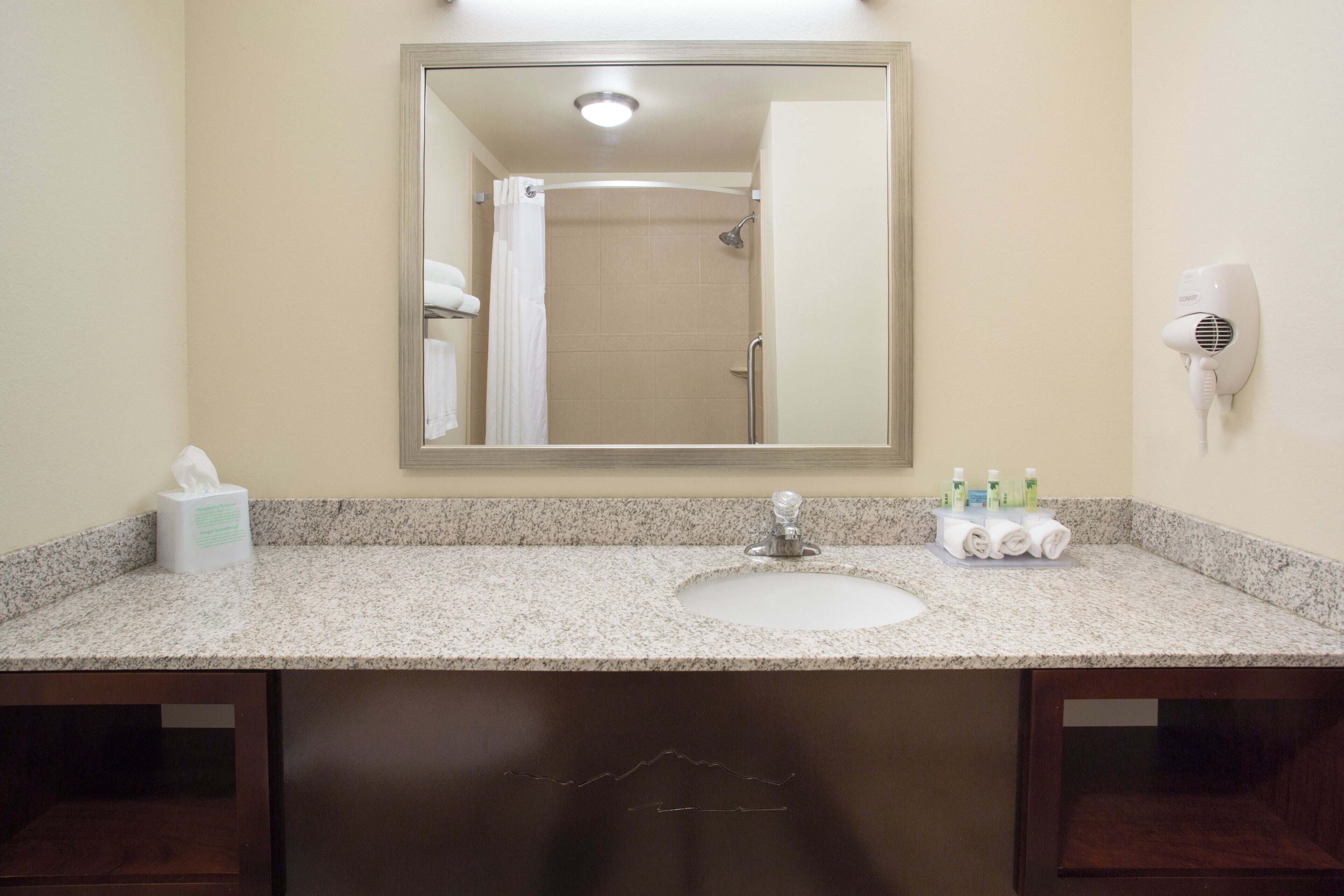 Une salle de bain équipée d’un lavabo, d’un miroir, d’un porte-serviettes et d’un sèche-cheveux fixé au mur.