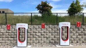 Two Tesla charging stations with a brick wall and a fence in the background. - Holiday Inn Express & Suites Glendive by IHG (Glendive)