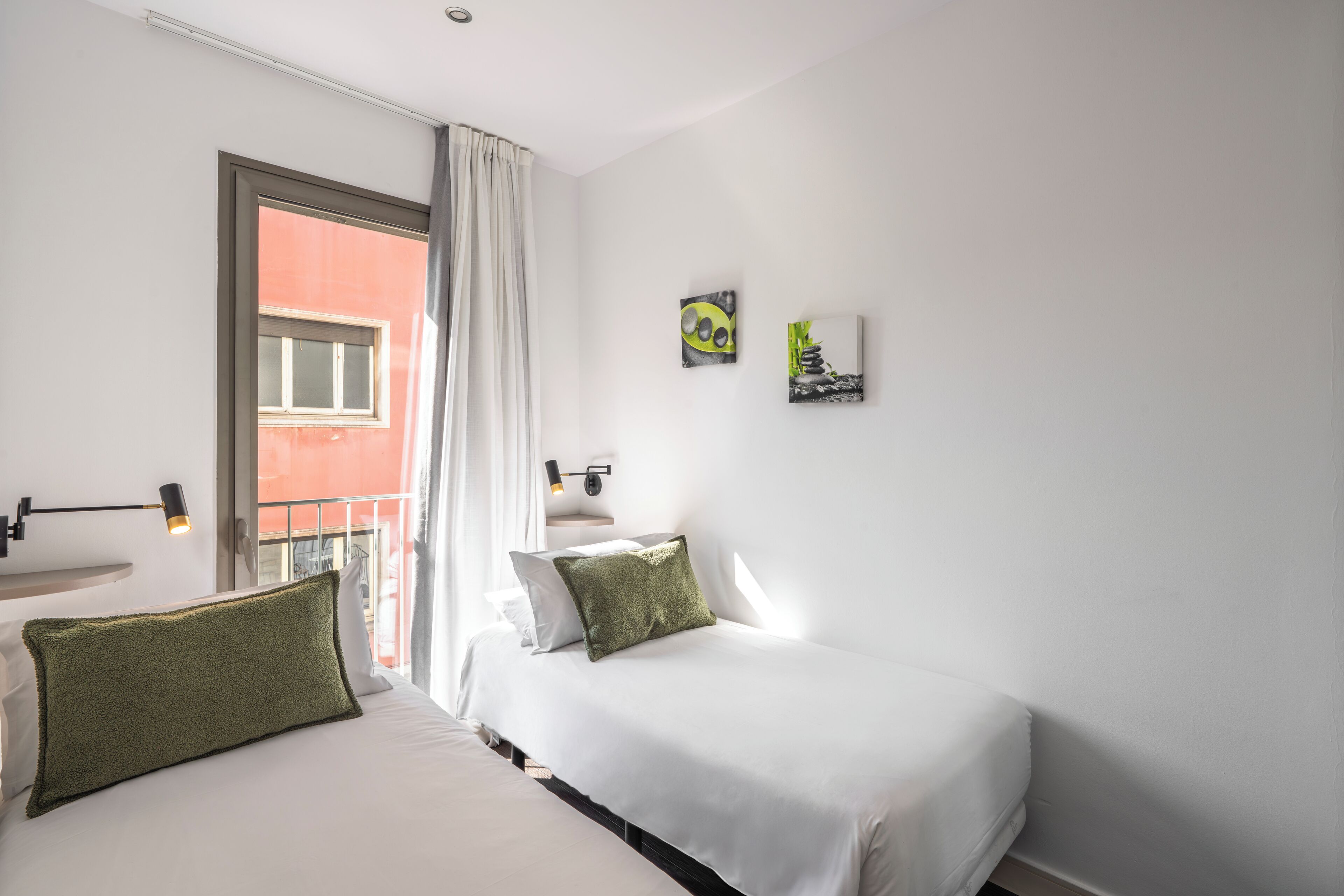 Een hotelkamer met een bed, een raam met gordijnen, een klein tafeltje en een kunstwerk aan de muur.