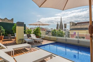 A rooftop pool area with lounge chairs and umbrellas, overlooking a cityscape with historic buildings. - Aspasios Catedral Apartments (Barcelona)
