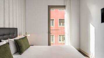 A hotel room with a bed, a nightstand, a lamp, and a view of a building through a window.