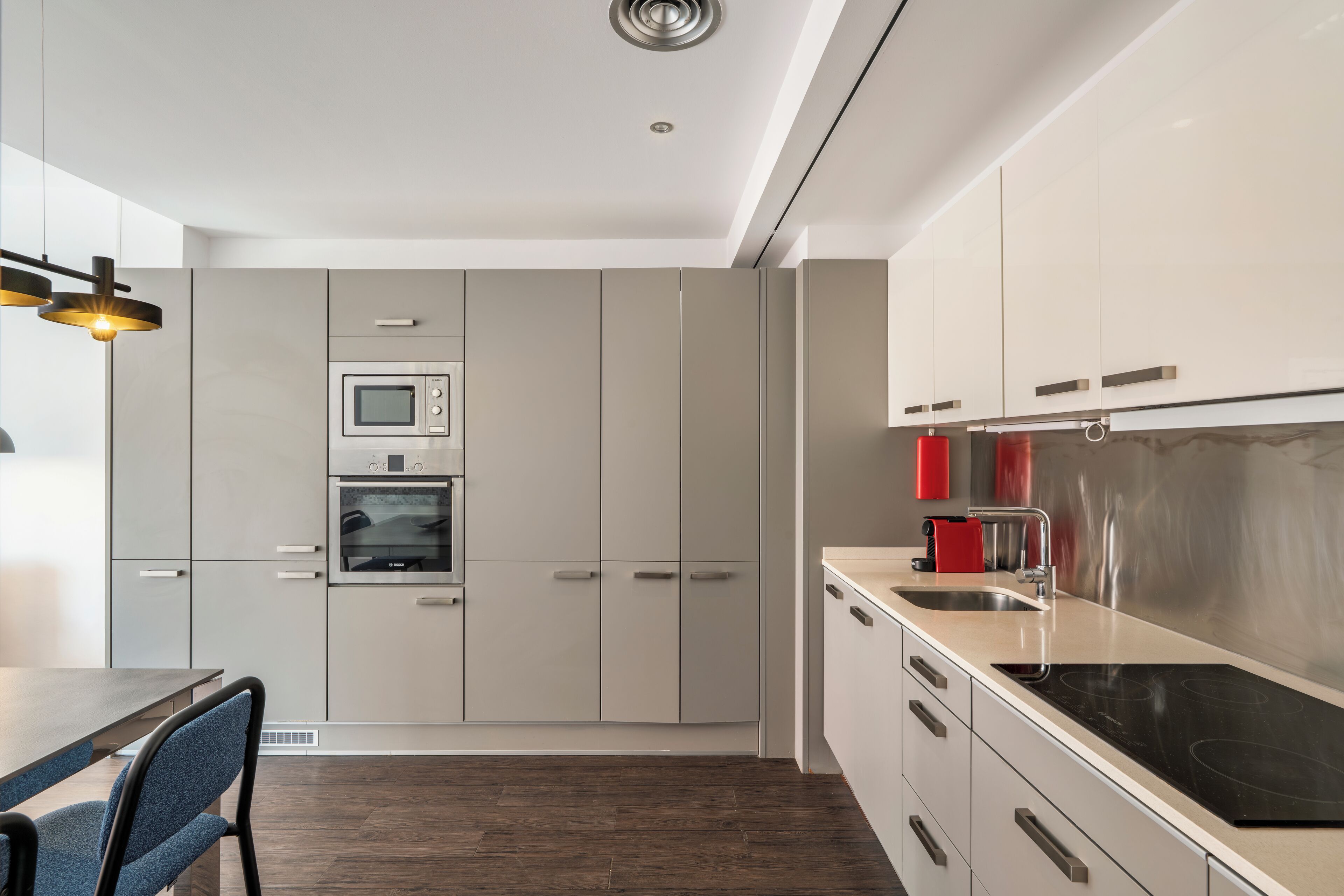 A modern kitchen with stainless steel appliances, white cabinetry, and a dark wood floor.