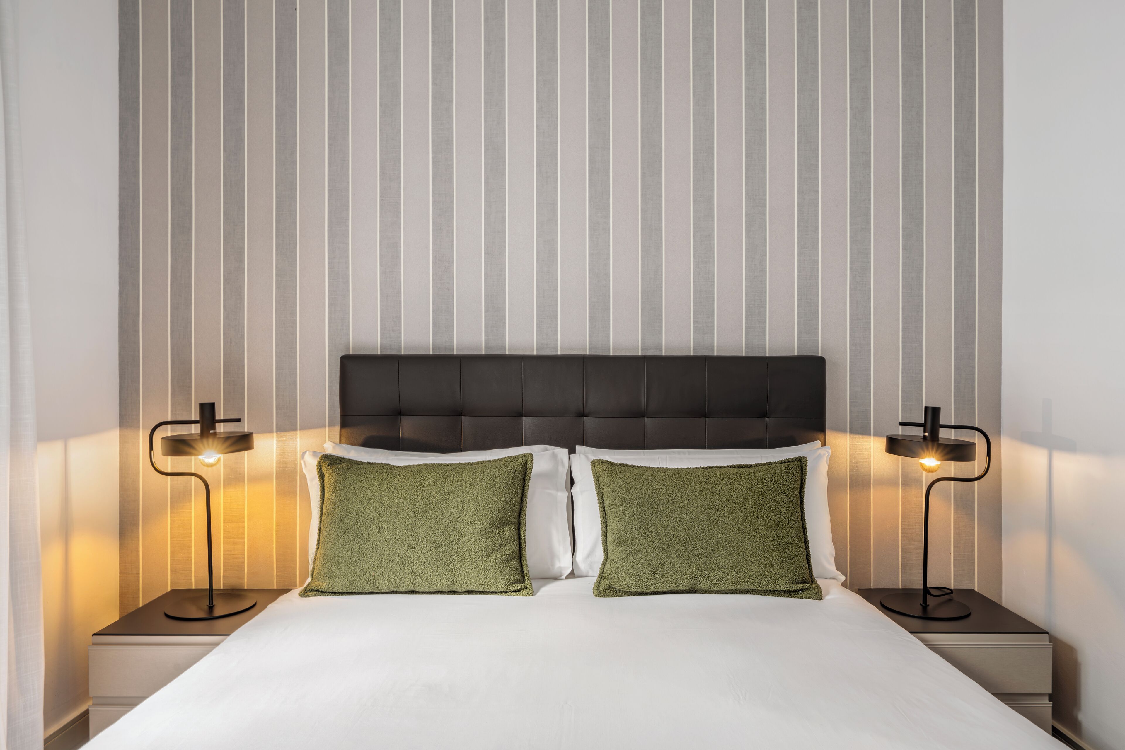 A neatly made bed with two pillows, a headboard, and two bedside lamps.