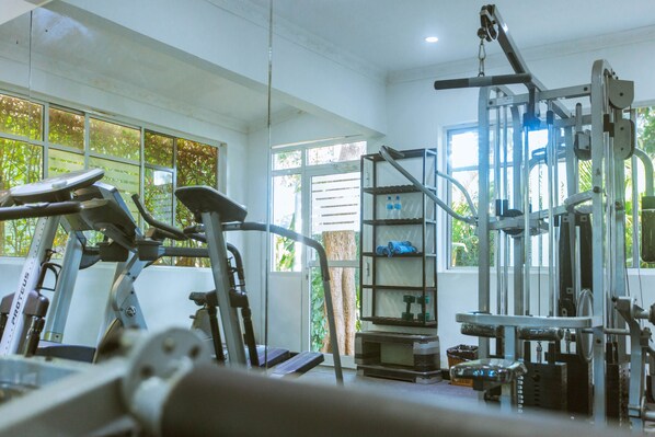 A gym with exercise equipment, large windows, and a view of greenery outside.