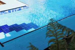 A swimming pool with blue tiles and a wooden deck area.