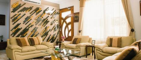Una sala de estar con dos sofás beige, una mesa de centro de vidrio y una pared decorativa con réplicas de murciélagos de madera.