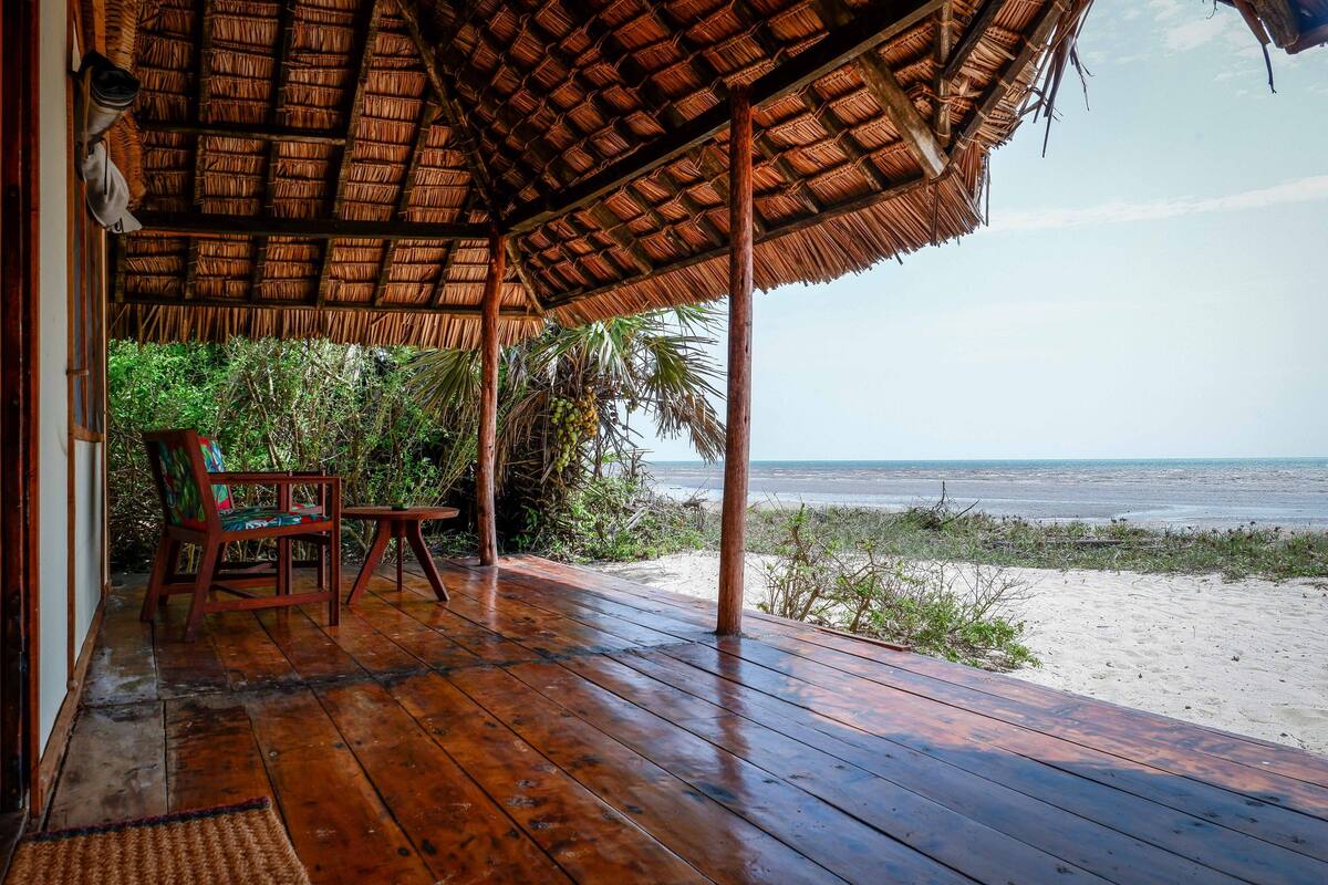 Una terraza de madera con techo de paja que da a la playa.