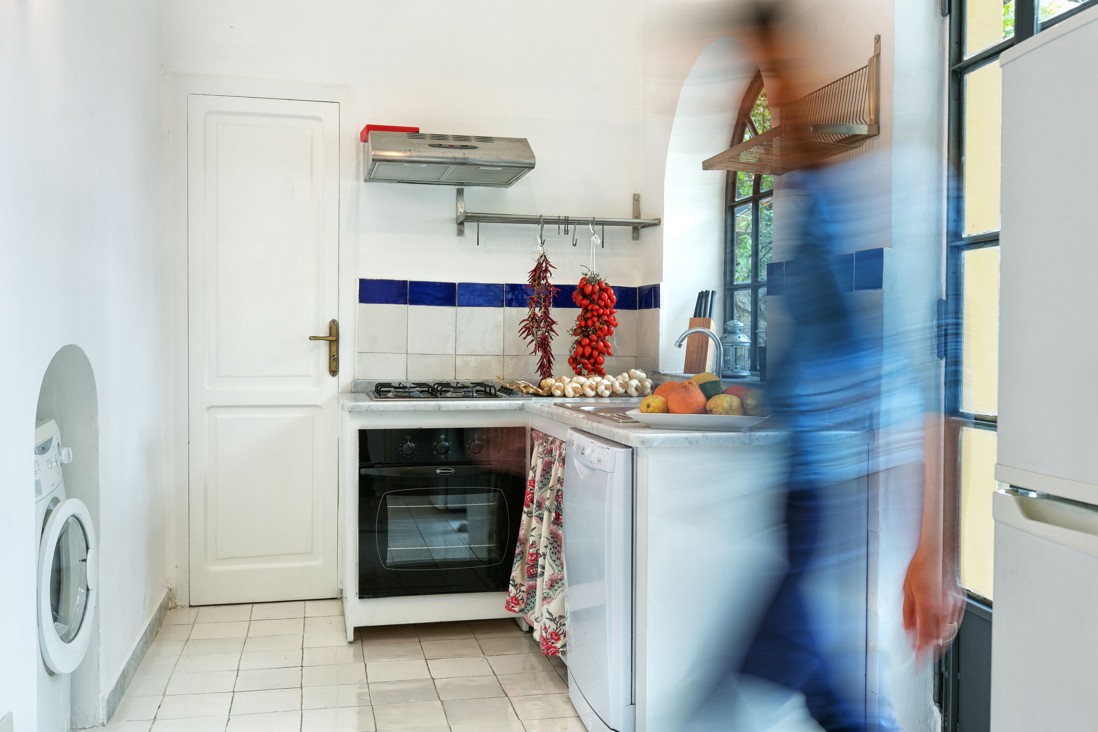 Una cocina con estufa, horno y verduras colgando.