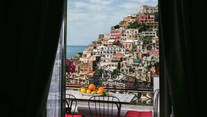 Un balcon avec des chaises rouges et une table, donnant sur une colline aux couleurs vives, parsemée de bâtiments, sous un ciel dégagé.