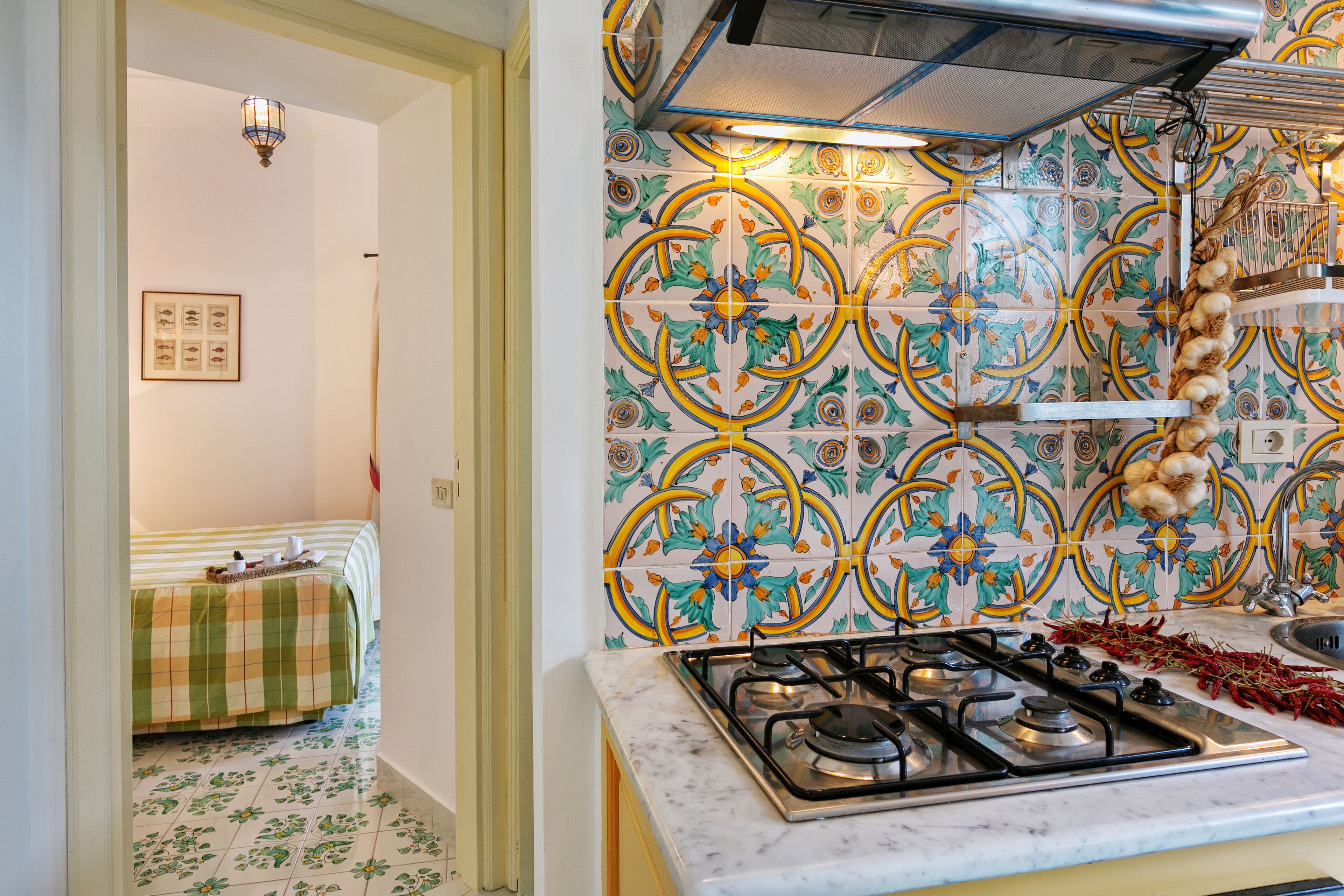 Una cocina con estufa a gas, salpicadero de azulejos y una zona de comedor con mantel a cuadros.