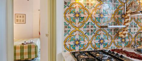 Una cocina con estufa a gas, salpicadero de azulejos y una zona de comedor con mantel a cuadros.