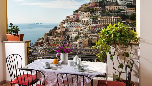 Une terrasse avec une table dressée pour le dîner, offrant une vue sur une ville côtière avec des bâtiments situés sur une colline.