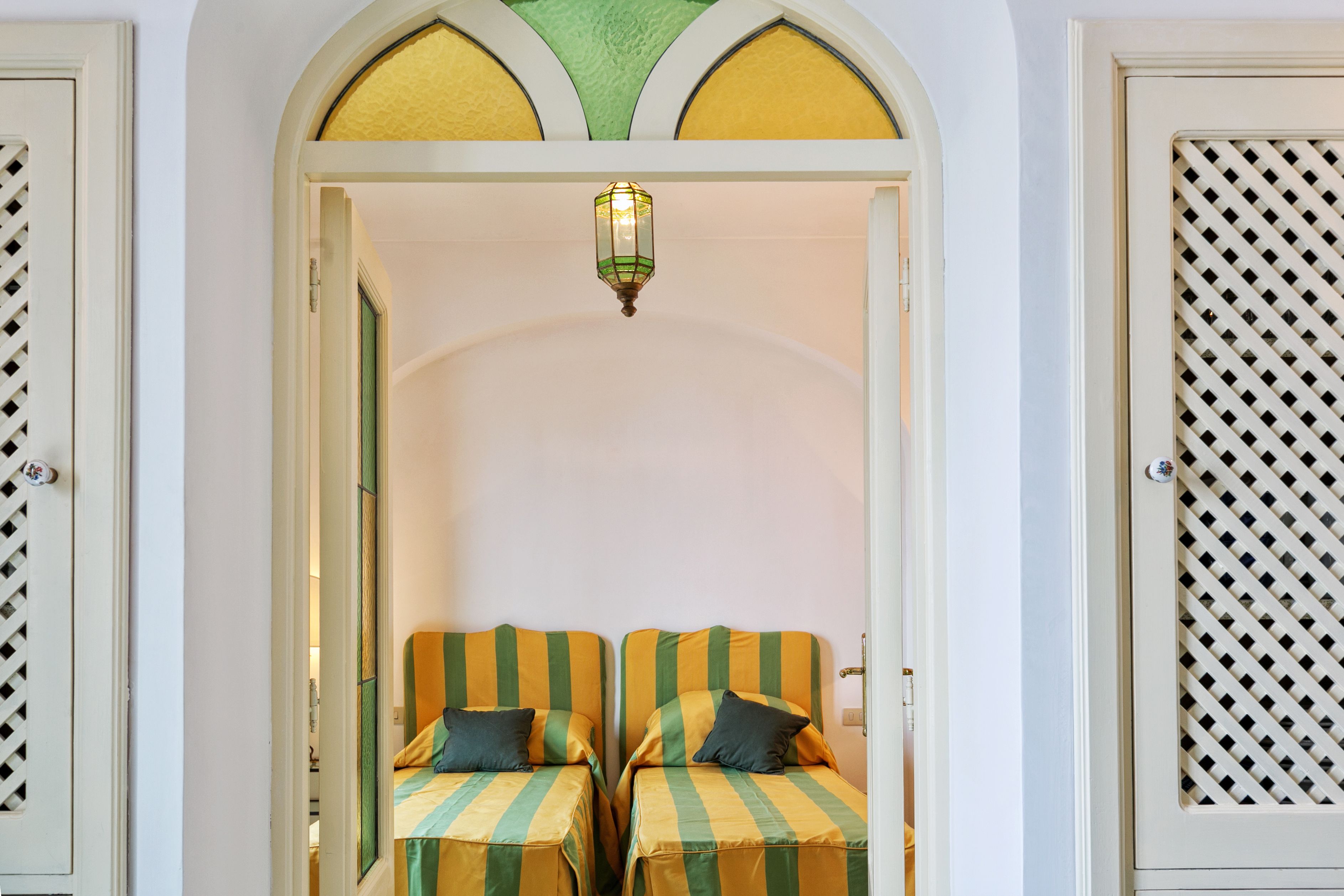 A room with two beds, a decorative archway, and a hanging light fixture.