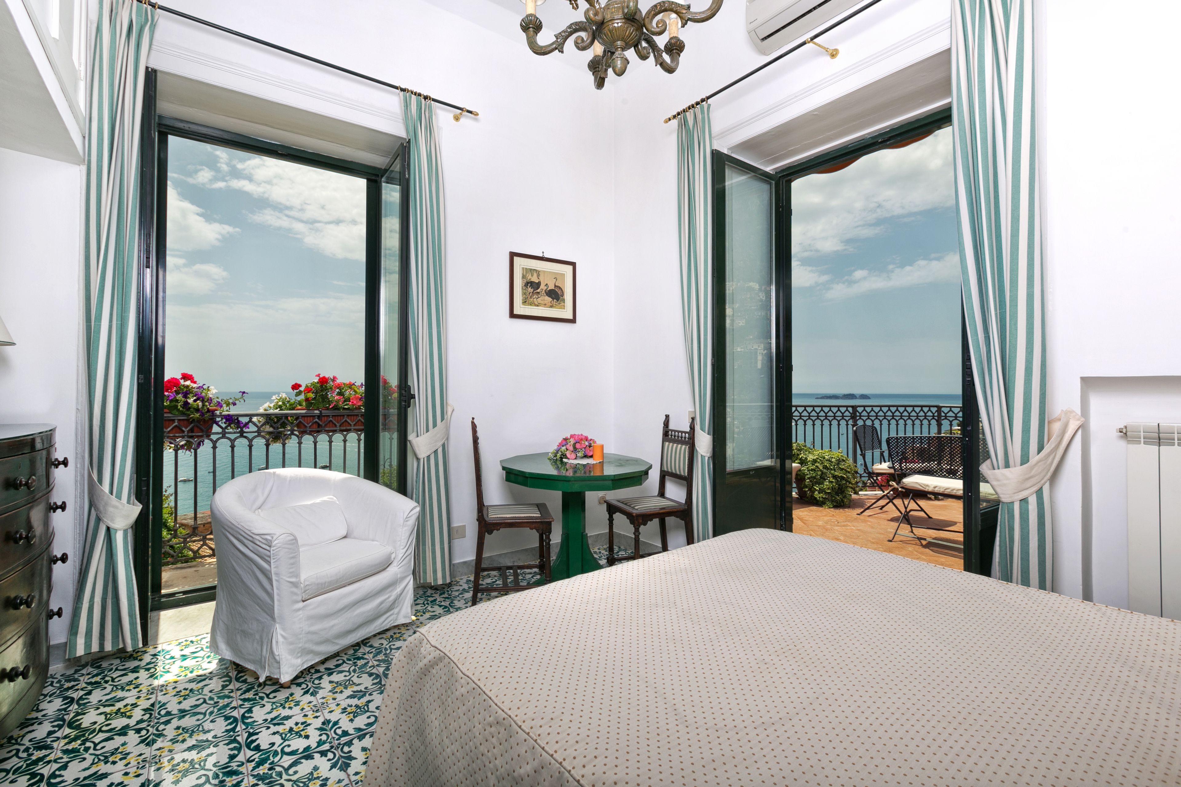 Habitación de hotel con cama, una mesita con sillas, balcón con vista al mar y una ventana con cortinas.