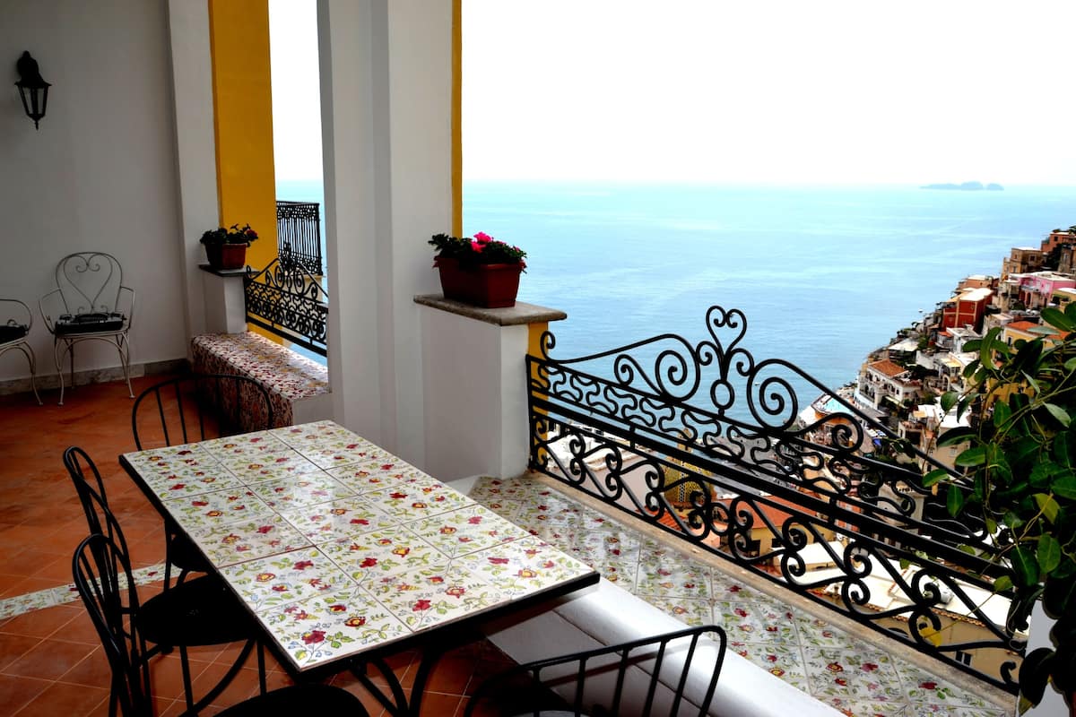 Un balcon avec une table et des chaises, une balustrade et une vue sur la mer.