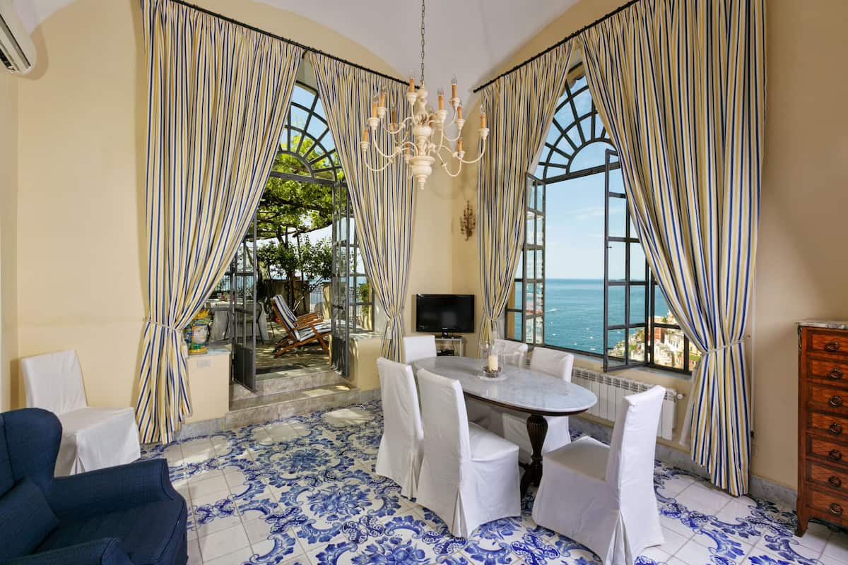 Une pièce comprenant une table à manger, des chaises, un téléviseur et donnant sur la mer.