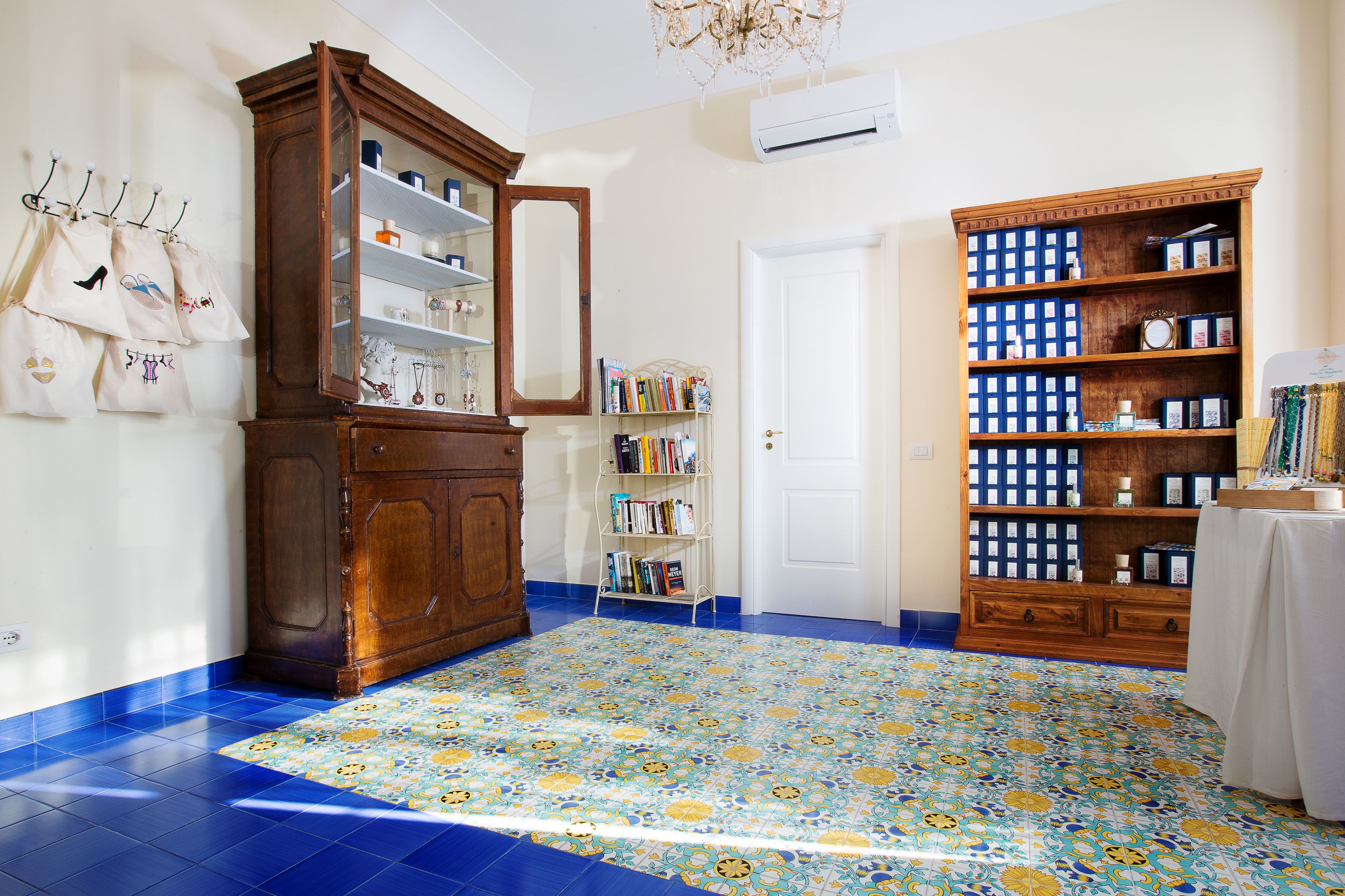 Una habitación con alfombra estampada, un aparador de madera con puertas de cristal, una estantería y una puerta blanca.