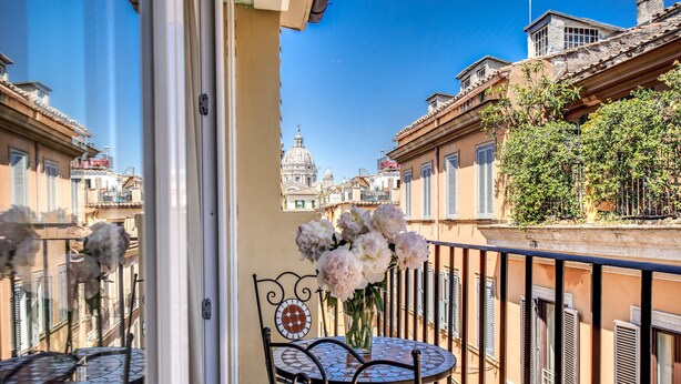A balcony with a round table and chairs, a vase of flowers, and a view of historic buildings. - Rome55 - Piazza di Spagna (Rome)