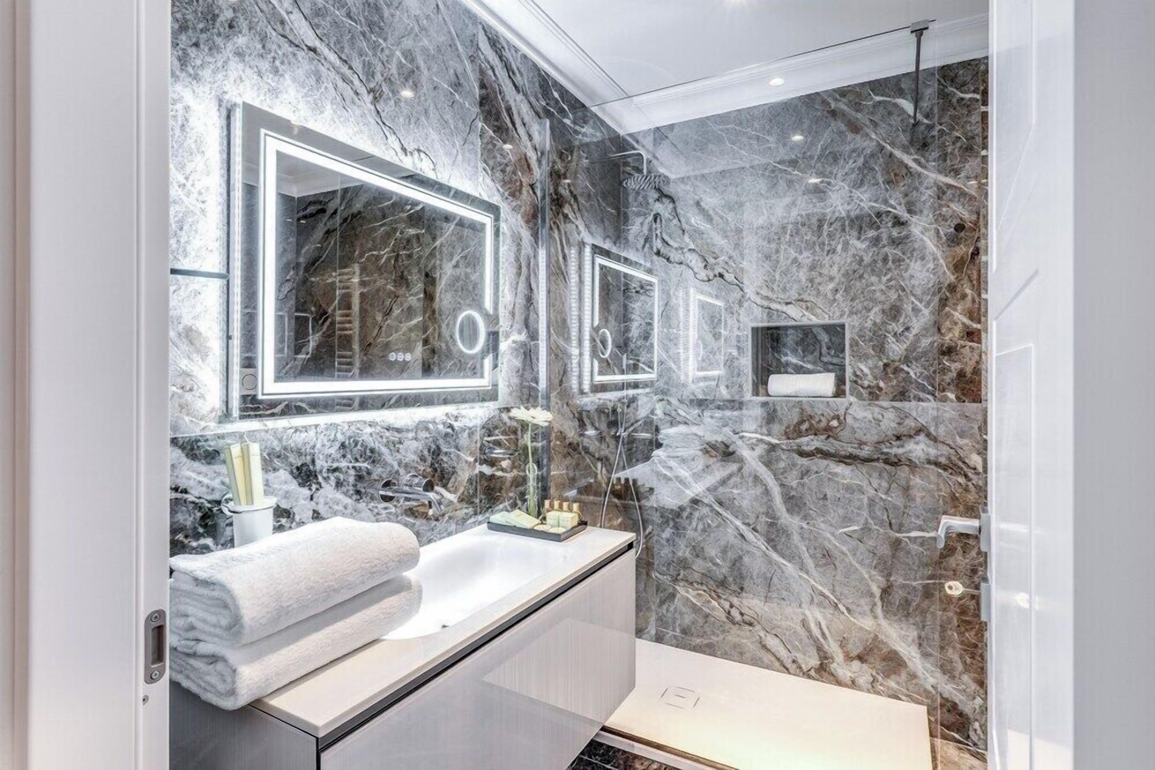 A modern bathroom with marble walls, a large mirror, and a white sink.