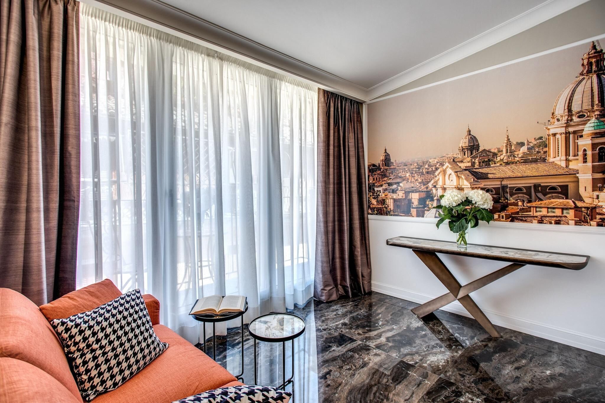 A modern living room with a sofa, a small table, and a view of a cityscape through sheer curtains.