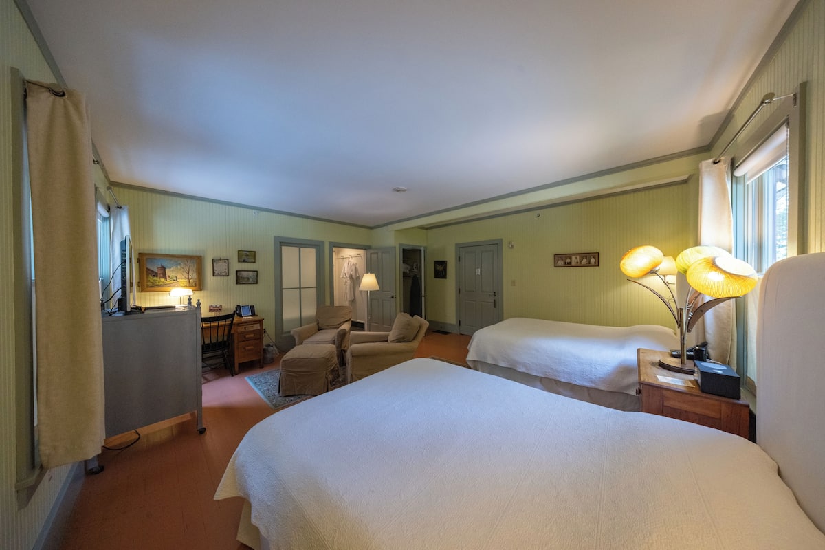 Une chambre d’hôtel avec deux lits, un bureau, une chaise et une lampe.