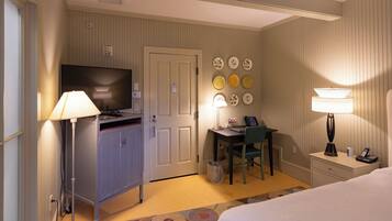 A hotel room with a bed, desk, chair, television, and wall-mounted lamps.